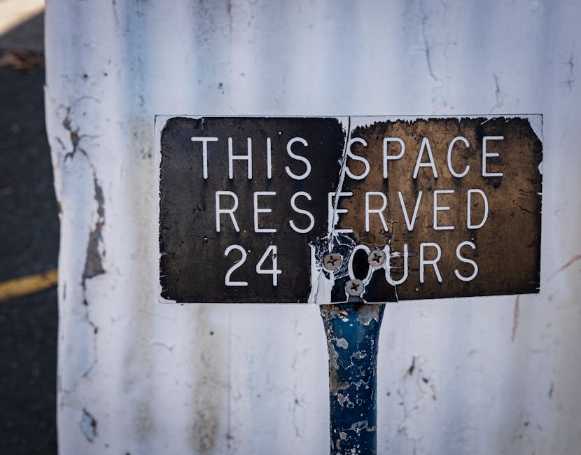 A weathered metal sign affixed to a rusted pole reads 'THIS SPACE RESERVED 24 HOURS' in white capital letters. The sign shows signs of aging, with peeling paint, rust, and corrosion, especially on the